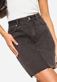 Černá džínsová sukně s třepeným lemem, má přední kapsu, poutka na opasek a kovové patentní zapínání v pase. Hladký povrch.