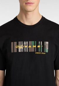 Sort bomulds T-shirt med et grafisk design med stænger i forskellige farver og teksturer, herunder grønne og brune nuancer, samt "VANS" i gul.