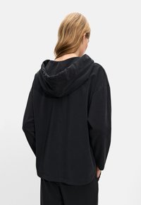Hanorac negru cu glugă și o croială lejeră. Material moale, mâneci largi și o cusătură centrală pe spate. Design minimalist, fără modele vizibile.