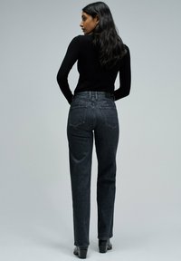 Vaqueros negros de tiro alto y pernera recta, con cinco bolsillos, textura sutil y una cintura ajustada. Llevados con una blusa de manga larga ajustada.