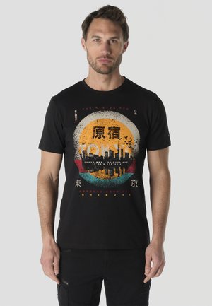 Hombre que lleva una camiseta negra con el skyline de la ciudad de Tokio y caracteres japoneses impresos sobre un fondo circular multicolor.