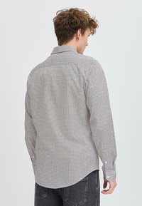 Camisa de manga larga de color blanco con un patrón geométrico negro, cuello abotonado y un dobladillo curvado. Fabricada en tela ligera.