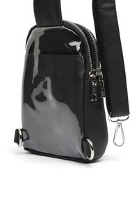 Borsa nera con un pannello frontale lucido, retro in pelle nera testurizzata, cerniere e accessori in metallo argentato ai lati.