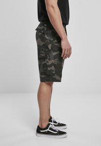 Cargo shorts in een donker camouflagepatroon, gemaakt van stof met een gestructureerde afwerking, voorzien van meerdere zakken en een rechte snit.