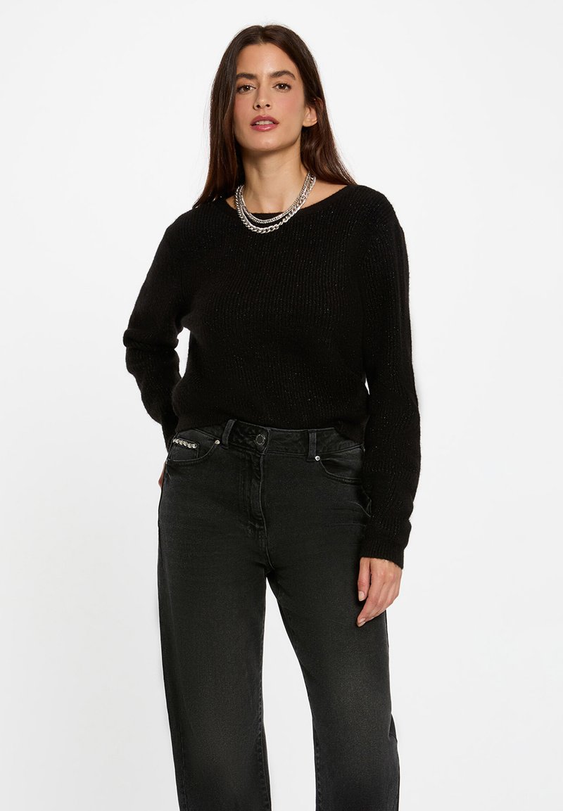 Maglione nero a maglia con scollo a barchetta e maniche lunghe, abbinato a jeans neri a vita alta con una leggera texture. Collana in catena d'argento come dettaglio.