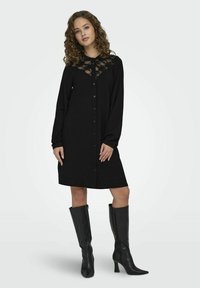 Czarna sukienka koszulowa z długimi rękawami, koronkowym wykończeniem przy dekolcie, miękka tkanina, do kolan, w zestawie z czarnymi botkami do kolan.