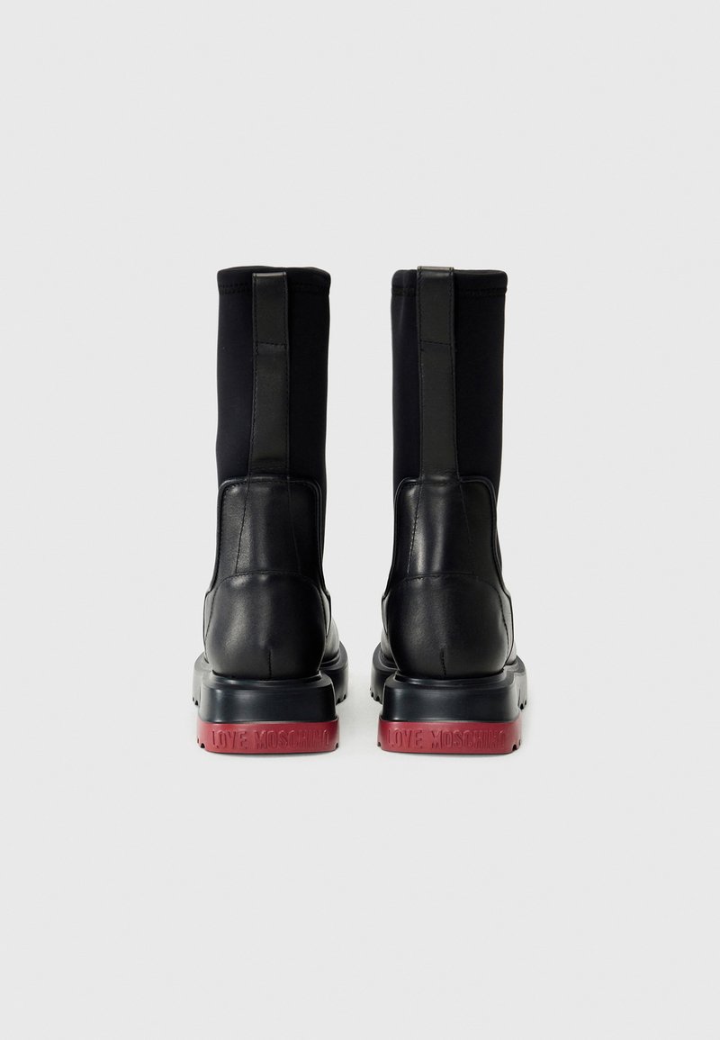 Stivaletti neri con un design in pelle liscia e tessuto, dotati di una suola nera spessa e del marchio rosso "LOVE MOSCHINO" sul tallone.