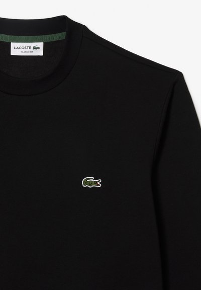 Sweatshirt noir en coton, avec un col rond. Logo crocodile brodé vert et blanc notable sur la poitrine gauche. Coupe classique.