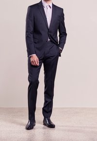 Marinsynt kostym med slim fit, snedrevade slag, enknappsstängning, i kombination med en ljus randig skjorta och svarta läderskor. Slät textur.