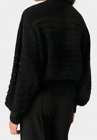 Schwarzer Strickpullover mit lockerer Passform, der über texturierte Muster und weite Ärmel verfügt. Rippbündchen und -saum verleihen dem Design zusätzliche Details.