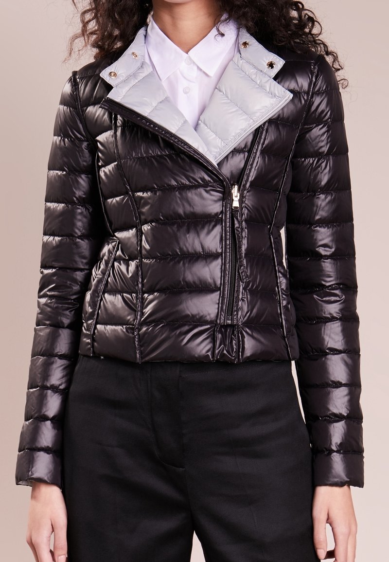 Chaqueta acolchada negra con un acabado brillante. Presenta un cuello gris en contraste, cierre de cremallera y secciones acolchadas horizontales. Textura brillante.