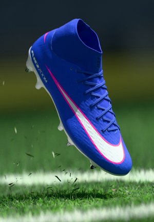 Blå fodboldstøvle med hvid og pink Nike swoosh, mid-cut design og Air Zoom-tekst over grøn græs på en bane.