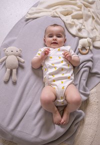 Coperta a maglia grigia chiara con un neonato in tuta bianca, decorata con motivi di limone gialli; un giocattolo orso all'uncinetto beige e un anello da dentizione in legno vicino.