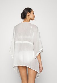 Weißes Leinen-Kaftan mit einem lockeren, fließenden Design; verfügt über weite Ärmel und einen zarten Saum entlang der Kante für zusätzliche Details.