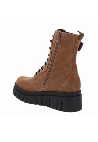 Bottines en daim marron avec une fermeture éclair sur le côté, semelle épaisse noire et détails en laçage, dotées d'une boucle à l'arrière pour un enfilage facile.