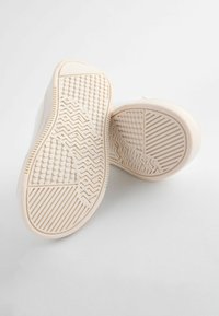 Baskets blanches avec une semelle en caoutchouc texturée arborant des motifs circulaires et en zigzag. L'intérieur présente une surface lisse et unie.