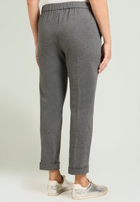 Pantalones grises entallados con textura suave, cintura elástica y puños doblados, combinados con zapatillas claras sobre un fondo neutro.