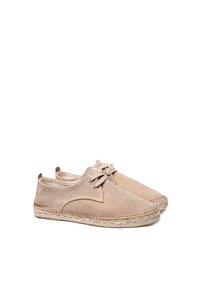 Scarpe in tela beige con punta rotonda, suola in juta intrecciata e chiusura con lacci. Presentano dettagli cuciti lungo i bordi e una texture morbida.