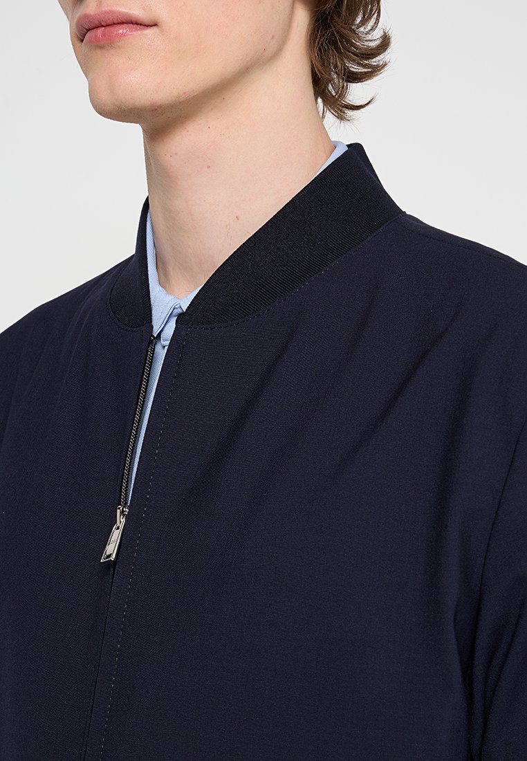 Marineblauer Bomberjacke mit geripptem Kragen, Reißverschluss und glatter Stoffstruktur, mit einem sichtbar hellblauen Innenfutter.