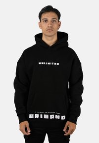 Sudadera con capucha negra hecha de material grueso, con texto blanco "UNLIMITED" en el pecho y "BRIGAND" con una frase en el área del bolsillo.