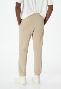 Pantaloni jogger beige realizzati in tessuto morbido, con tasche laterali, polsini elasticizzati e una vita comoda. Indossati con scarpe bianche.
