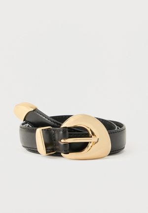 Ceinture en cuir noir enroulée avec une grande boucle irrégulière brillante en or et une pointe dorée sur fond blanc.