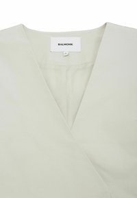 Jasnoszara bluzka wrap z dekoltem w kształcie litery V, wykonana z gładkiego materiału. Posiada metkę z napisem "BALMOHK" oraz oznaczenie rozmiaru. Prosty, minimalistyczny design.