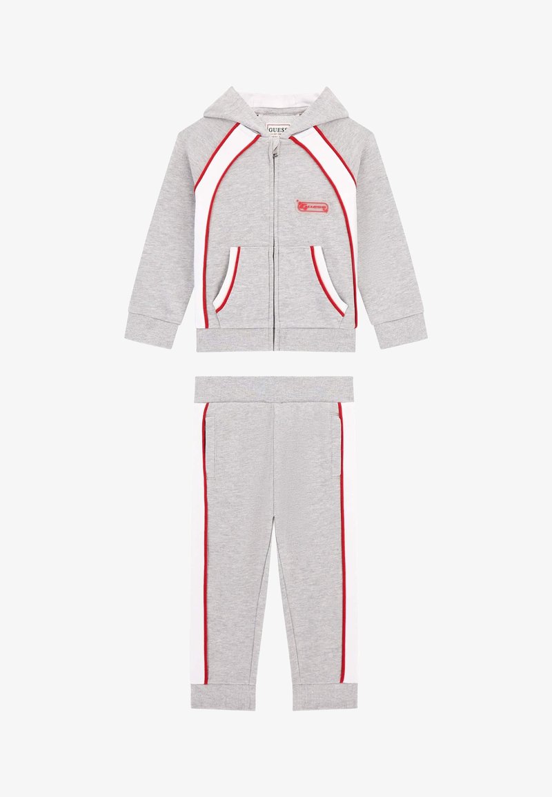 Šedý športový teplákový komplet s kapucňou na zips a červenými a bielymi detailmi, klokanka kapsami a zodpovedajúcimi joggermi so bočnými pruhmi.