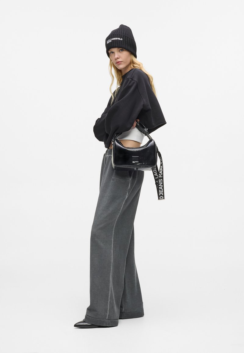 Fekete cropped pulóver, szürke bő szárú nadrág, fekete kötött sapka, és fényes fekete kézitáska ellentétes pánttal és ezüst kiegészítőkkel.