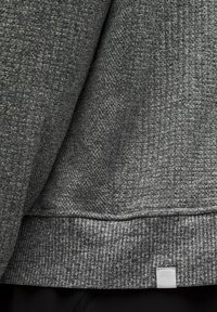 Pelēks teksturēts džemperis ar audumu rakstu, ribotām piedurknēm un mazu logo uzšuvumu apakšmalā. Mīksts audums ar strukturētu dizainu.