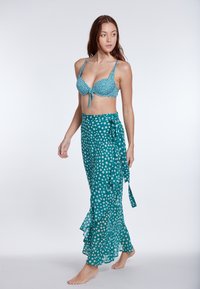 Jade bikini top s pikastimi in zavezovanjem ter ujemajoča zavita krilka z nabranim robom, oba izdelana iz lahkotnega materiala.