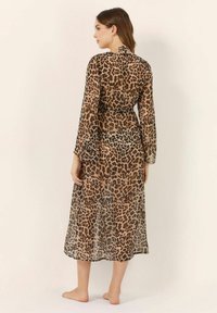 Leopardi-kuosiset, läpikuultavat pitkähihaset mekko, jossa on solmittava kaula-aukko, virtaava siluetti, joka ulottuu puoliväliin pohkeita, ja jossa on pehmeä, kevyt rakenne.