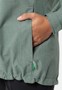 Giacca in tessuto verde chiaro e testurizzato con tasca laterale e orlo inferiore elasticizzato. Presenta una zip grigia e dettagli con etichetta verde.