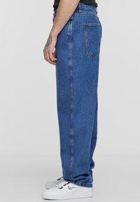 Mėlynos džinsinės kelnes su laisvu prigludimu, pasižyminčiomis aukštu liemeniu, tiesiomis kojomis ir galiniais kišenėmis. Sukombinuota su baltomis sportinėmis bateliais.