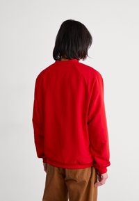 Red sweatshirt with a high collar, long sleeves, and a relaxed fit. Smooth fabric texture, no visible patterns or hardware.