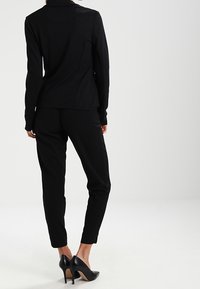 Blazer nero aderente e pantaloni tapered, entrambi realizzati in tessuto liscio. La giacca ha un colletto, mentre i pantaloni presentano una vestibilità slim. Scarpe con tacco alto.