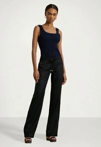 Mujer de pie vistiendo un top sin mangas de punto azul marino, pantalones de pierna ancha negros con cordón y sandalias de plataforma azul marino.