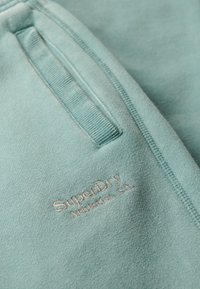 Sudadera de algodón azul claro con cuello acanalado, pequeño bolsillo delantero y logotipo bordado "SuperDry Athletics, CA". Textura suave.