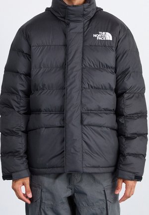 Mann trägt eine schwarze Steppjacke mit hohem Kragen und dem The North Face Logo auf der Brust, kombiniert mit dunkelgrauen Cargohosen.