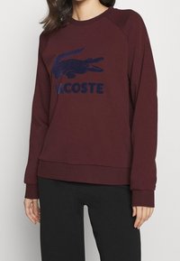 Sweatshirt bordeaux en coton, avec un grand logo crocodile bleu marine et le texte "LACOSTE", doté de poignets et d'un ourlet côtelés.