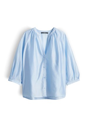 Blouse bleu clair à manches longues avec col en V, boutonnage sur le devant, et légers fronces aux épaules et aux poignets, présentée à plat sur fond blanc.