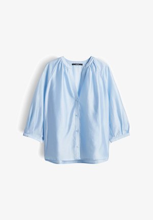 Blouse bleu clair à manches longues avec col en V, boutonnage sur le devant, et légers fronces aux épaules et aux poignets, présentée à plat sur fond blanc.