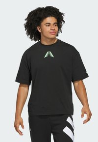 Czarna koszulka z krótkim rękawem, wykonana z bawełny, z odblaskowym zielonym trójkątnym logo na klatce piersiowej i luźnym krojem.