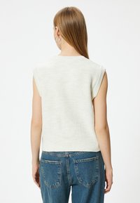 Pull en tricot sans manches de couleur crème clair, avec un col et un ourlet côtelés, associé à un jean taille haute bleu avec des poches arrière.