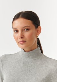 Sivi rebrasti pulover s visokim ovratnikom, uparen s zlatnim kružnim naušnicama. Glatka tekstura i minimalistički dizajn.