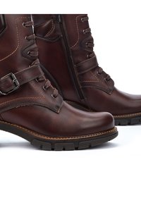 Brown leather ankle boots featuring a smooth finish, side zipper, lace-up design, stitching accents, and textured rubber sole.