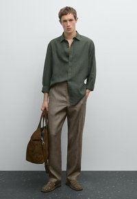 Green linen shirt with button closure, brown textured trousers, green sandals, and brown suede bag. Plain background.