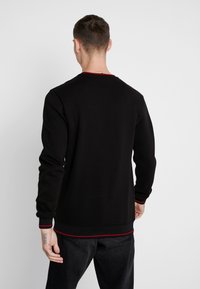 Sudadera negra de manga larga, con puños de canalé y un acento rojo en contraste a lo largo del escote y el dobladillo. Textura de tela suave.