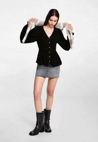 Black long-sleeve blouse with a V-neck and buttons, paired with a gray denim mini skirt and black ankle boots. Sweater draped on shoulders.
