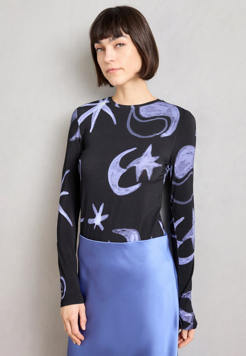 Τοπ με μακριά μανίκια σε μαύρο ύφασμα με μοτίβα ουράνιου θόλου σε μωβ, συνδυασμένο με απλή φούστα από απαλό γαλάζιο σατέν. Απλός λαιμός, εφαρμοστή γραμμή.